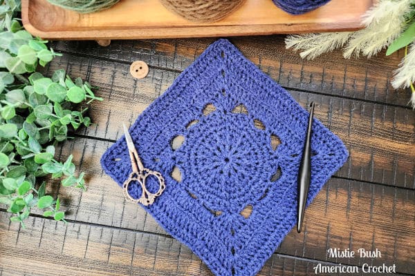 The Fritzella Square crochet pattern laid flat with a skein of worsted weight yarn and a 5.5mm hook, ready for crafting.